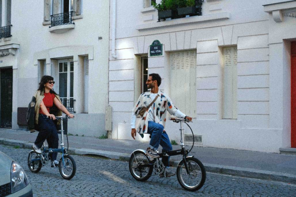Man and a women riding two folding e-bikes in a historic city street